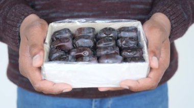 Adam elinde bir kutu hurma meyvesi tutuyor. ,