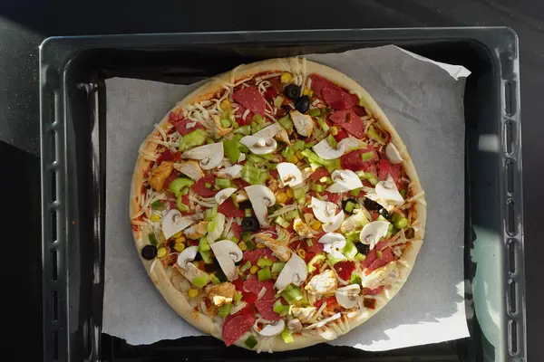 A loaded pizza on a pan with various toppings, a delicious fast food dish.
