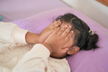 a upset child girl cover her face with hand .