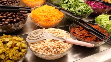 Zeytin, fasulye, havuç, marul ve biraz daha marul içeren çeşitli taze malzemelerle dolu bir salata barına yakın plan..