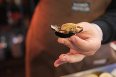 A person is holding a recently opened mussel at a seafood market, emphasizing its freshness and quality for sale clipart