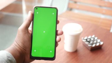 Yeşil ekranlı akıllı telefon ve masada bir fincan kahve. ,