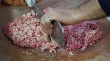 Yakın plan bir görüntüde, yemek hazırlamak için mutfak tezgahında et ve baharatları karıştıran eller görülüyor.