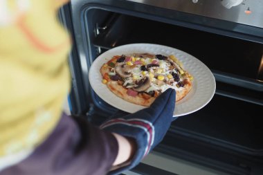 Ev yapımı pizzayı fırına koyan kişi emniyet eldiveniyle pişirmeye hazır. Hevesli aşçı.