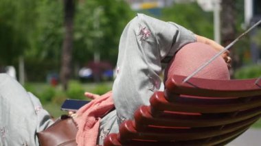 Huzurlu bir anın tadını çıkaran kişi güzel yeşil bir park ortamında ahşap bir bankta uzanır..