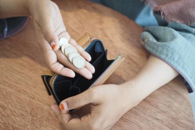 Elinde bozuk para tutan bir kadın, açık bir cüzdanın yanında, ahşap bir masaya yerleştirilmiş.