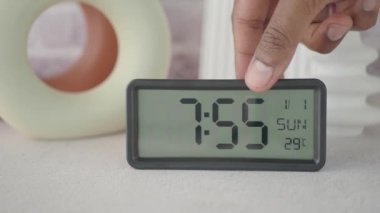 Arka planda dekor öğeleri olan bir masadaki dijital alarm saati ayarlanıyor.
