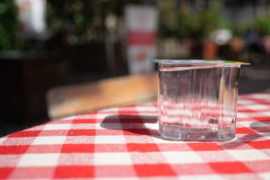 Dışarıdaki kareli masada plastik bardakta su, kırmızı ve beyaz masa örtüsünde cam bardak..