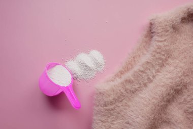 Plastik kaşıkta yıkama tozu ve masada pembe renkli bir bez. .