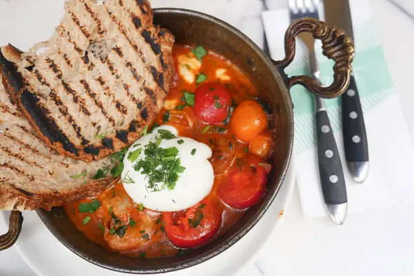 Shakshuka ziyafeti, ızgara ekmek, taze otlar ve lezzetli bir yemek için krema.