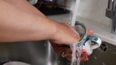 Bulaşıkları akan suyla yıkayan, günlük işleri yapan ve temizliği sürdüren kişi.