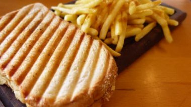 Ahşap bir tahtanın üzerinde patates kızartması ve sos ile nefis ızgara panini. Rahatlatıcı yemek.