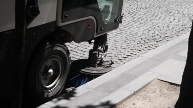 Güneşli bir günde kaldırım taşlı bir yolu fırçalayan ve temizleyen sokak temizleme aracı..