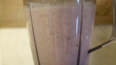 Bir insan sıvı içecek yapmak için mutfak aletini kullanıyor. Smoothie üretmek için yiyecek, su ve diğer malzemeleri harmanlıyorlar.
