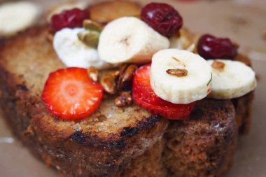 Dilimlenmiş muz, çilek, fındık ve kuru yaban mersinli Fransız tostu..