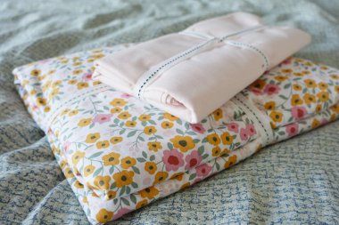 Katlanmış çiçekli ve katı çarşaflı yatak örtüsü yatak odasında huzurlu bir atmosfer yaratır.