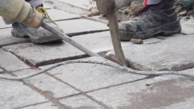 İki işçi inşaat alanındaki beton levhaları kaldırmak için matkap ve aletler kullanıyor..
