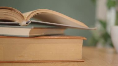 Yeşil bir arka plana karşı ahşap bir masa üzerinde sayfaları dönen açık bir kitap.