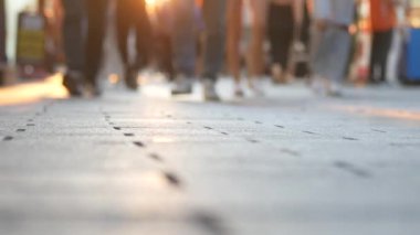 Akşam ışığında yürüyen yayalarla dolu işlek bir şehir kaldırımının yakın görüntüsü.