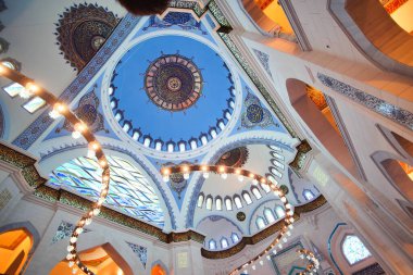 Karmaşık tasarım, mavi kubbeler ve zarif ışıklandırma içeren güzel dekore edilmiş bir cami tavanı..