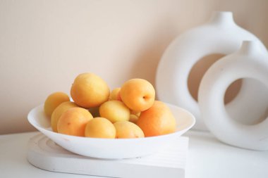 Taze kayısılarla dolu beyaz bir kase, modern dekorlu minimalist bir arka plana ayarlı..