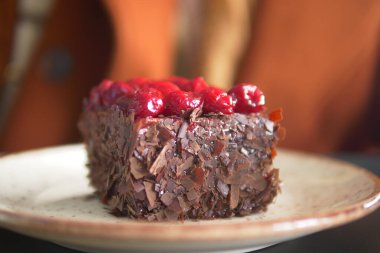 Beyaz bir tabakta kirazla kaplı zengin bir çikolatalı pasta diliminin yakın çekimi..