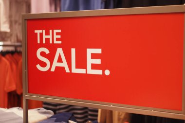 Bir giyim mağazasında parlak kırmızı satış tabelası, cesur metin ve satış etkinliğiyle müşterileri cezbediyor.