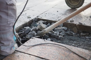 Şehir kaldırımını aletler ve ağır ekipmanlarla tamir eden bir inşaat işçisinin yakın görüntüsü.
