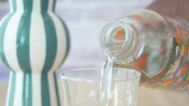 Yakın plan bir perspektif suyu şişeden bardağa akarken yakalar, bu da hidrasyon kavramını sembolize eder.