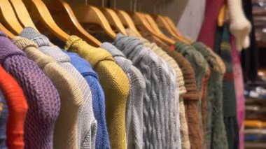 Bir butik giyim mağazasındaki ahşap askılara düzgünce asılmış renkli örgü süveterler..
