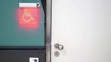 Tekerlekli sandalyeye erişimi gösteren kırmızı engelli işareti olan beyaz bir kapı..