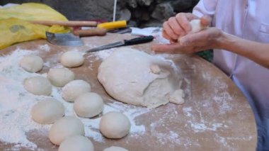 Fırıncı un kaplı bir yüzey üzerinde merdane kullanır, geleneksel mutfak tekniğinde el işi becerilerini gösterir.