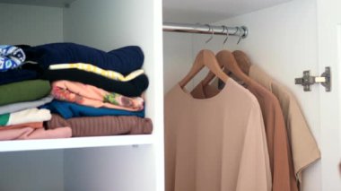 Raflarda düzgünce katlanmış giysiler ve ahşap askılarda asılı giysiler..