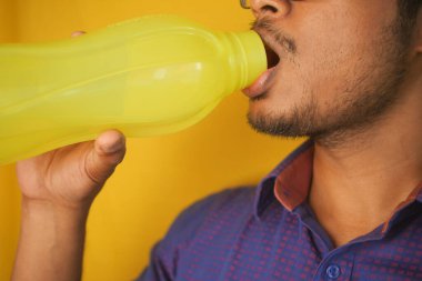 Sarı bir şişeden içen genç bir adamın yakın plan fotoğrafı..