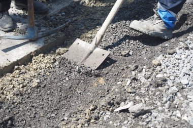 İşçiler yol kenarındaki çukura atmak için taşları kürekle alır. ,