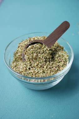 Kurumuş kekik baharatıyla dolu ahşap bir kepçe, deniz mavisi yüzeyine saçılmış, aşçılık için mükemmel..