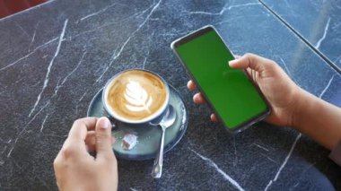 Elinde bir fincan kahve ve yeşil ekranlı akıllı telefon vardı. .