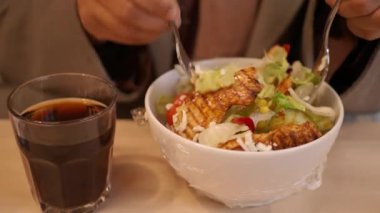 Taze ızgara tavuk salatasının tadını çıkaran kişi, ferahlatıcı bir içecekle sağlıklı bir akşam yemeği yakalıyor..