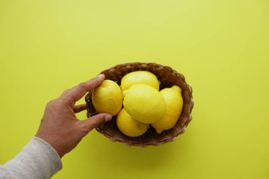 Bir el, parlak sarı arka planda duran taze sarı limon sepetine uzanır..