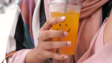 Gülen suratlı bir bardağı elinde tutan, neşeli ve rahat bir hava taşıyan bir kadının yakın çekimi..