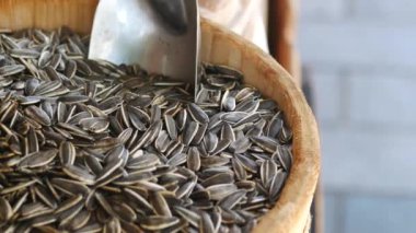 Ayçiçeği tohumlarıyla dolu ahşap bir sepet, metal bir kepçeyle birlikte bir pazarda sergileniyor.