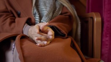 Sıcak bir ortamda oturan, sıcak bir palto ve eşarp giyen, kucağında katlanmış bir insan elleri..