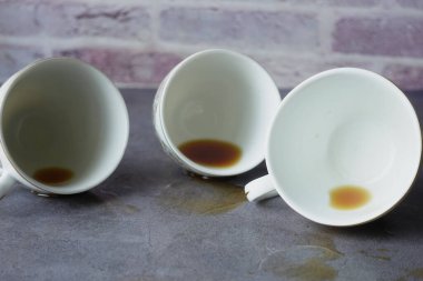 İçinde kahve kalıntıları olan üç beyaz kahve fincanı, tuğla kaplı bir masanın üzerine yerleştirilmiş..