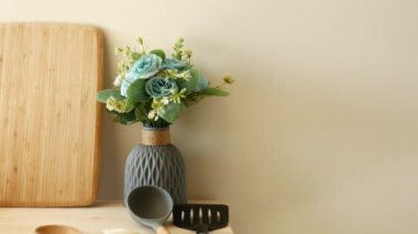 Çiçek vazosu, ahşap kesim tahtası ve pişirme aletleri içeren şık bir mutfak düzeneği..