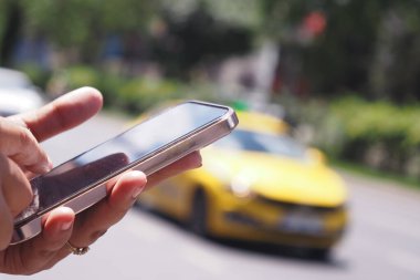 Bir kişi, şehrin kalabalık caddesinde taksi çağırmak için akıllı telefonu kullanıyor.