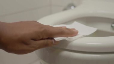 Birisi tuvalet kenarlarını titizlikle temizlemek için temizleme bezi kullanıyor.