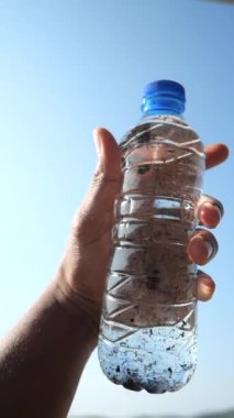 Mavi gökyüzüne karşı kirli bir yemek şişesi tutuyor. ,