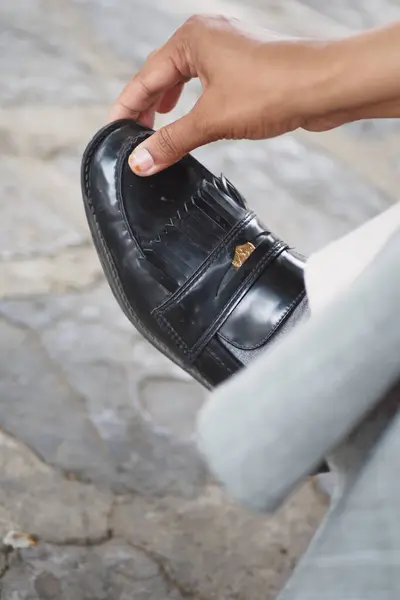 stock image Close-up of a hand adjusting the strap of a polished black leather dress shoe on a stone pavement.