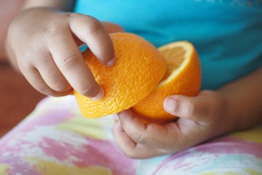 Bir çocuğun elleri canlı, taze kesilmiş turuncuyu tutuyor, parlak renklerini sergiliyor