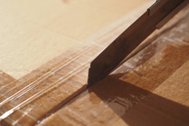 Bu, bir karton kutunun bandını ustalıkla kesen keskin bir bıçağın detaylı yakın plan görüntüsü.